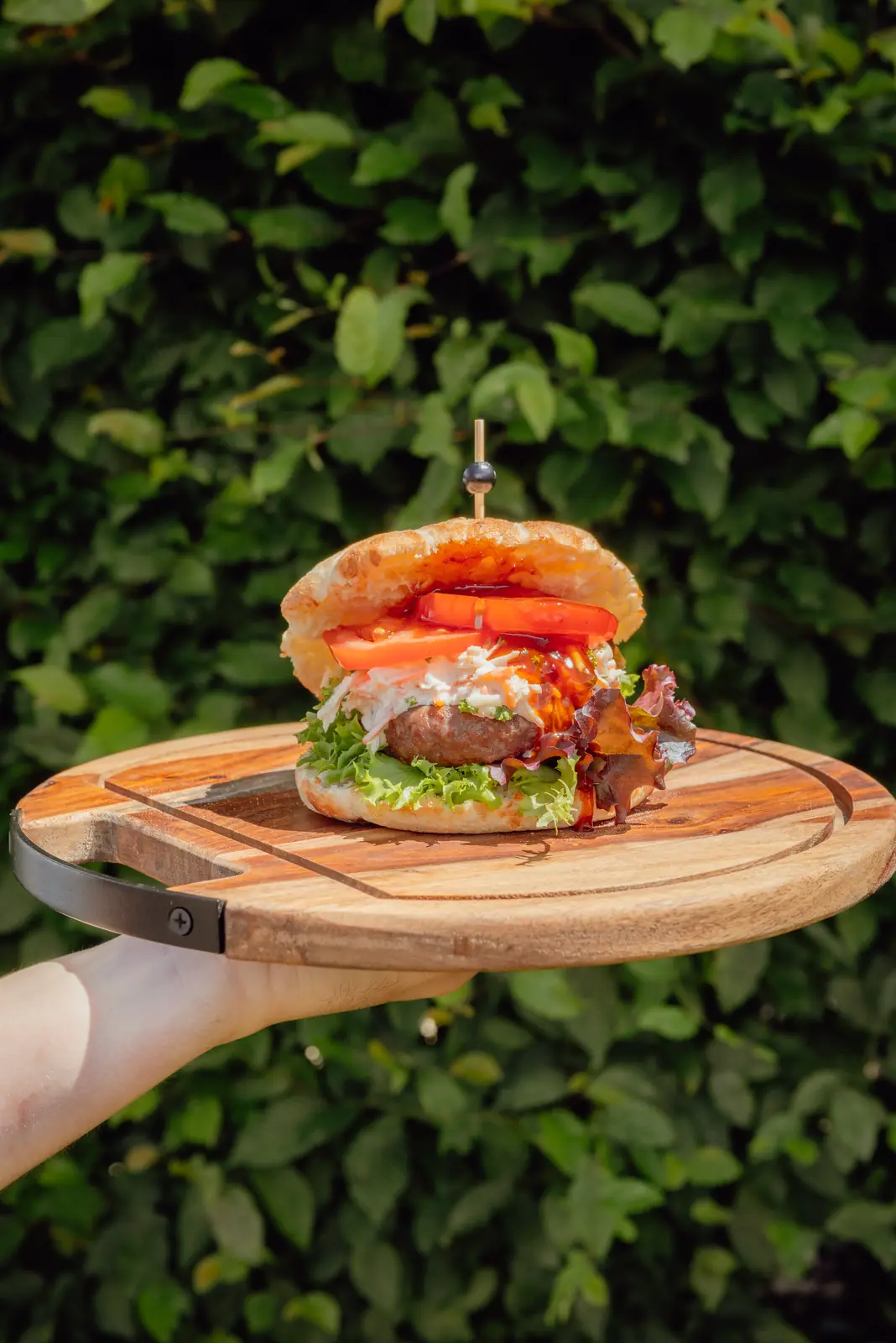 Black Angus burger op een houten plank, voor een groene haag