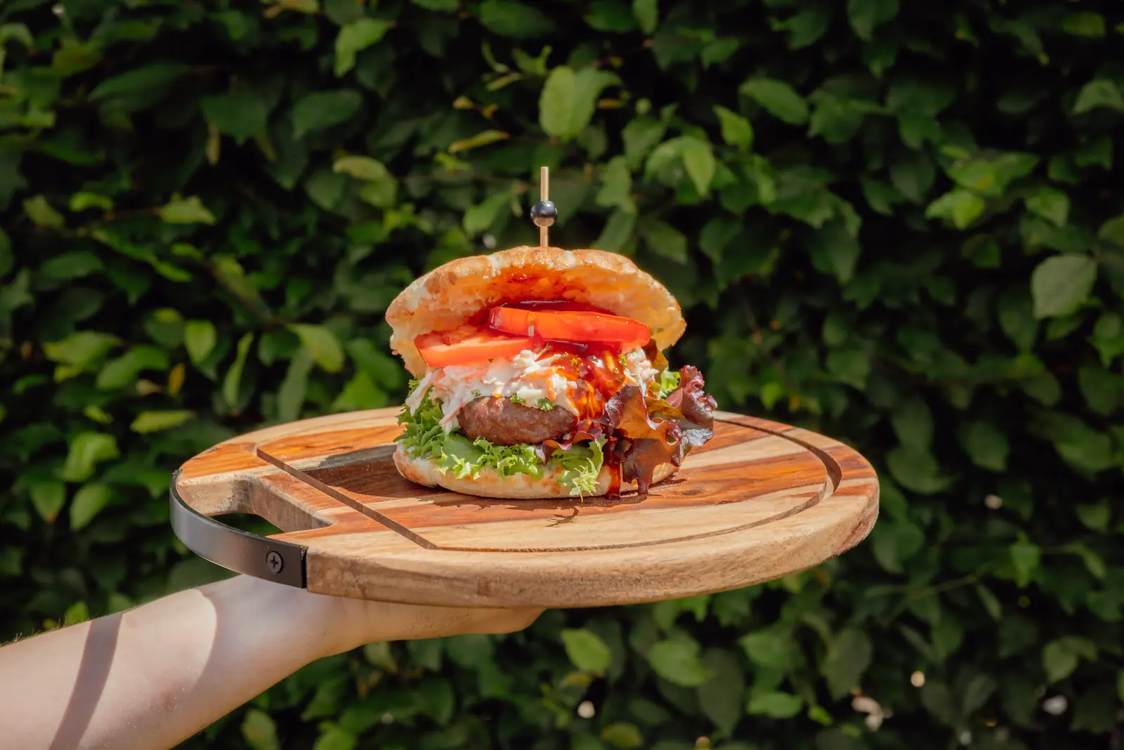Black Angus burger op een houten plank voor een groene haag