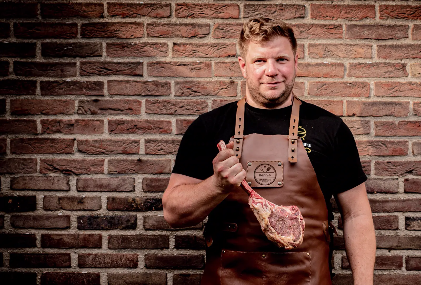 Hendrik van Hennie's BBQ met een tomahawk voor een bakstenen muur