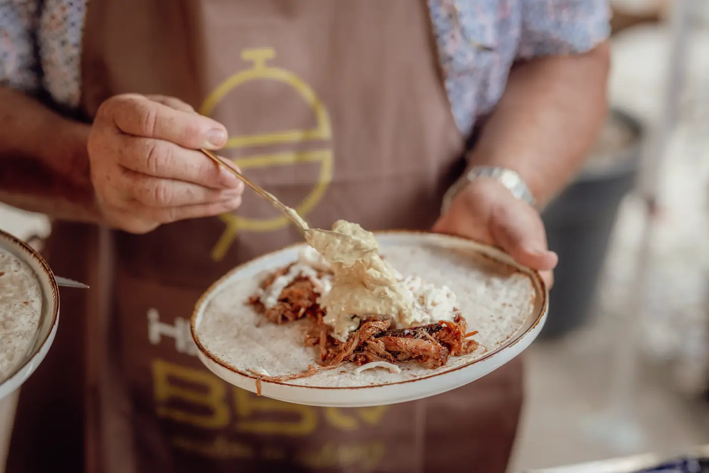 Een bord met pulled meat, vastgehouden door iemand in een schort van Hennie's BBQ